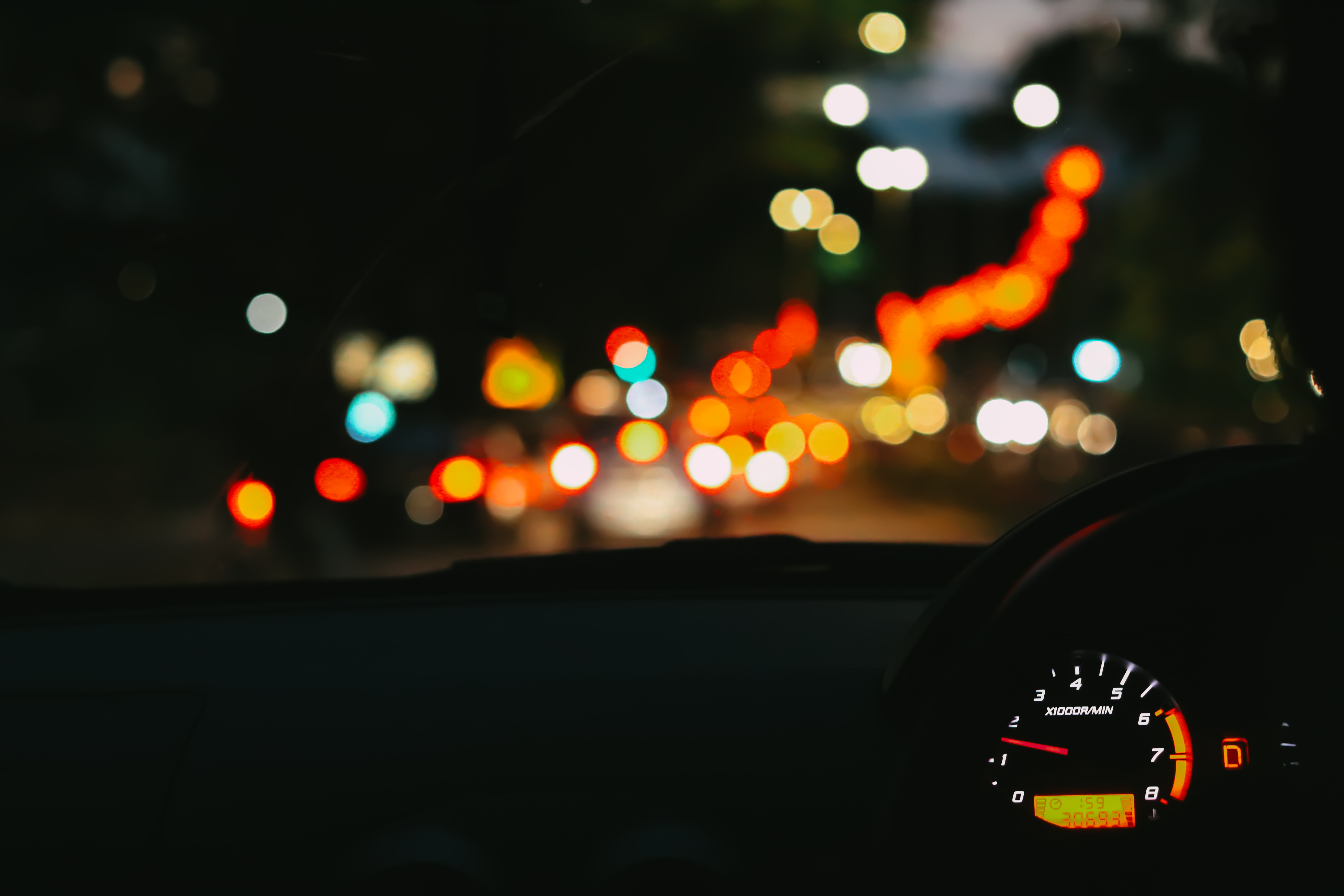 A car dashboard with a speedometer and a blurry street lights.